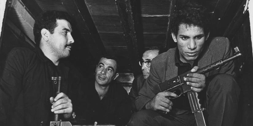 Four men, two armed with automatic rifles, huddle closely in the back of a truck.