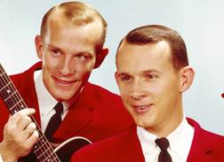 Dick and Tom Smothers with a guitar and harp in their hands and red jackets on in The Smothers Brothers Comedy Hour