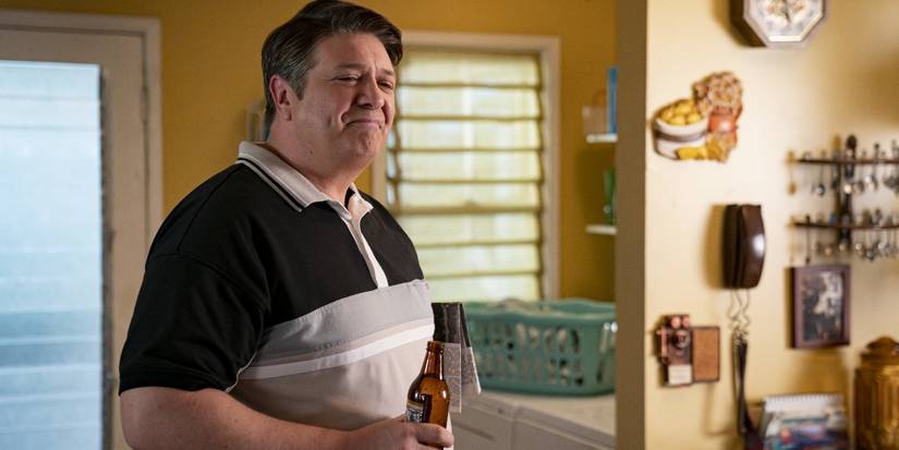 Lance Barber as George Cooper Sr. with a beer in hand smiling at something off-screen in Young Sheldon