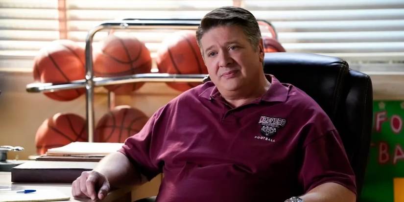 Lance Barber as George Cooper Sr, sitting his office with a rack of basketballs behind him in Young Sheldon