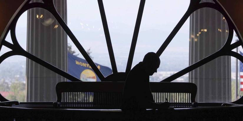 A silhouetted man writes something down in front of a paned window in his office, in Dark Money (2018).