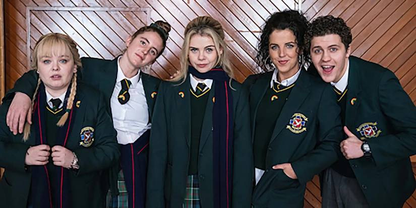 The cast of Derry Girls pose in uniform against a wooden wall