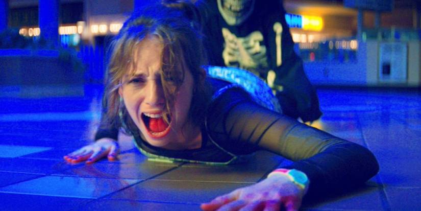 A girl being pulled across the floor by a man in a skeleton outfit, bathed in blue light.