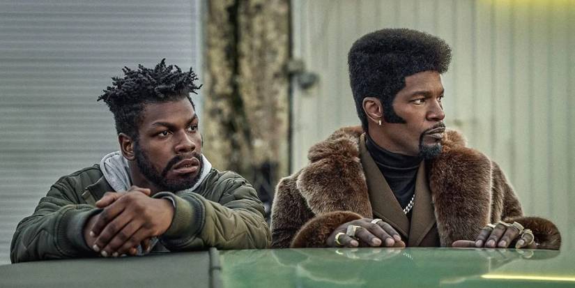 John Boyega and Jamie Foxx leaning on a car in They Cloned Tyrone