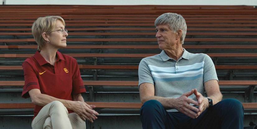Matthew Modine sits with a woman in the bleachers above a sports field in Operation Varsity Blues: The College Admissions Scandal (2021).