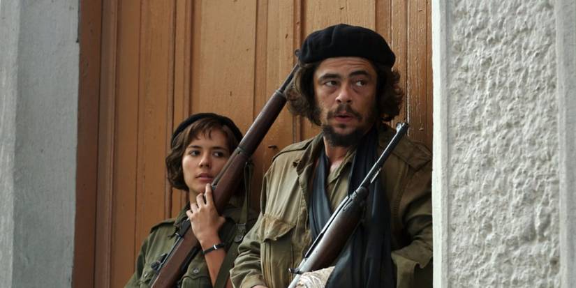 Benicio Del Toro in Che (2008), leaning against a door with a rifle in hand