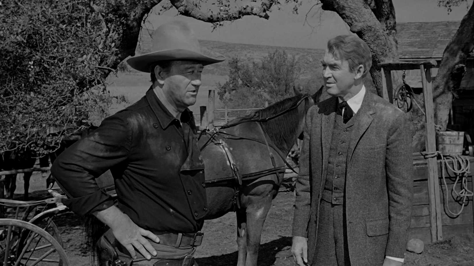 James Stewart and John Wayne talking in front of a horse in The Man Who Shot Liberty Valance