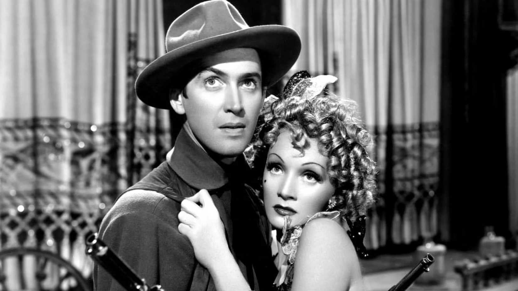 James Stewart embracing Marlene Dietrich as he brandishes two guns in Destry Rides Again