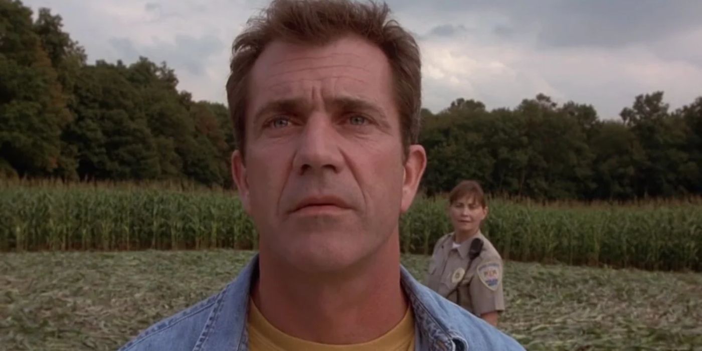 Mel gibson looks at the sky while a police officer stands behind him in a crop field in the film signs