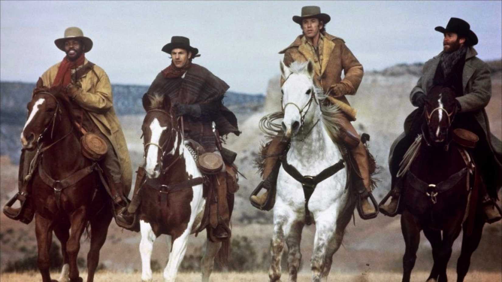 The cast of Silverado movie riding on horses through an open grassland area 