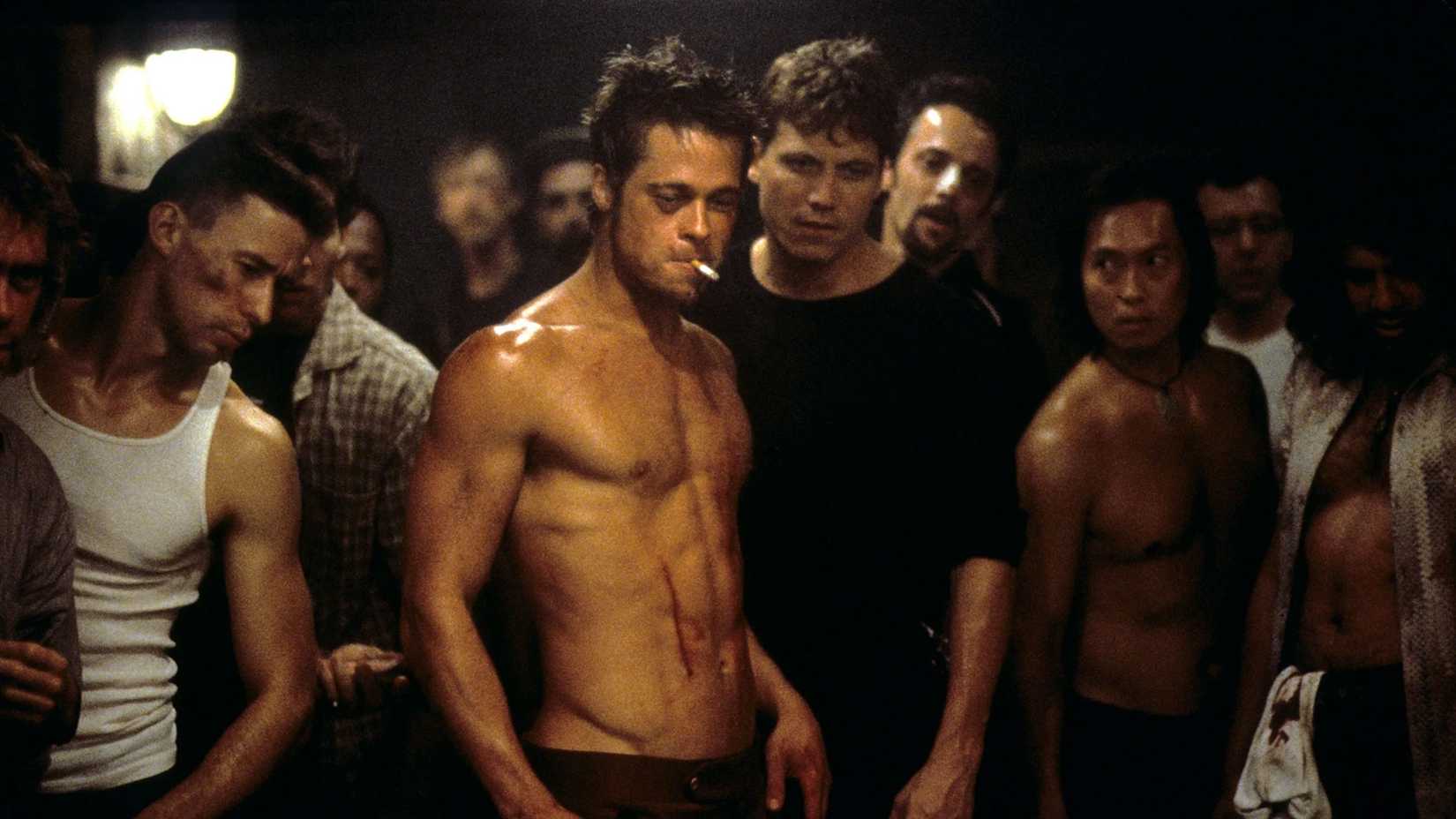 Tyler Durden, covered in bruises and smoking a cigarette, surrounded by a group in Fight Club.