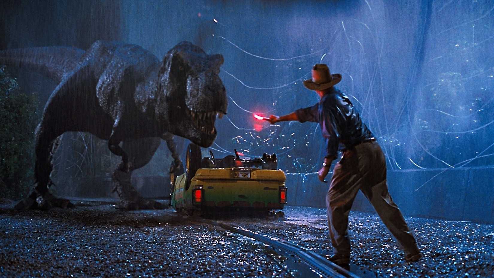 Sam Neill as Alan Grant in Jurassic Park waving a flare in front of a T. rex