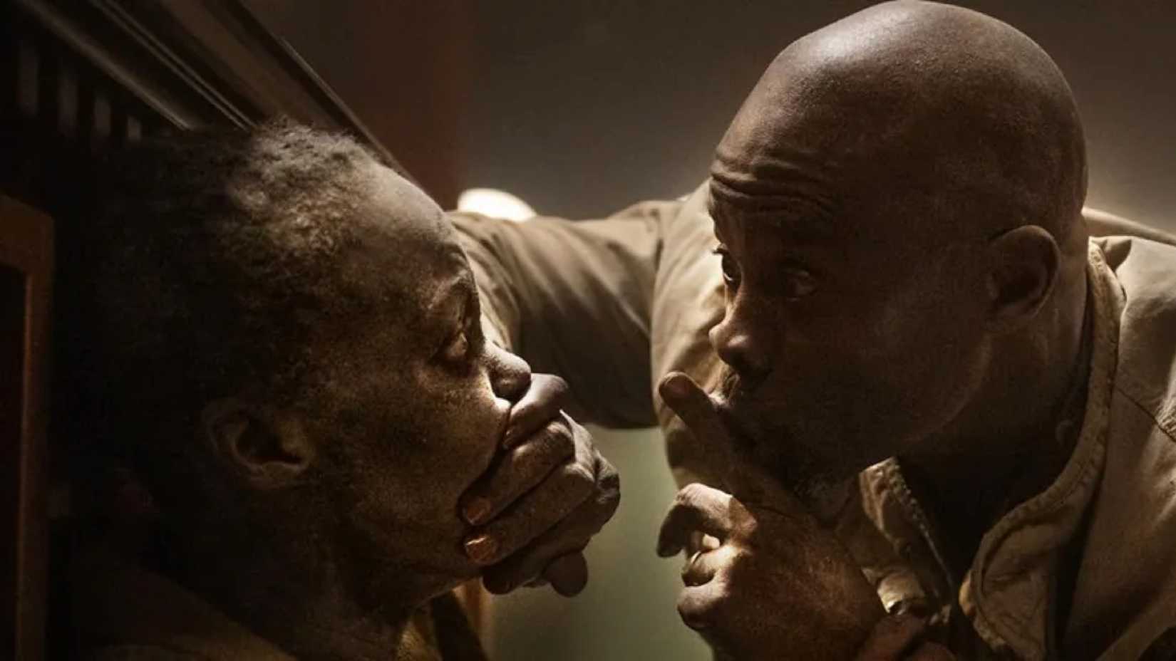 Lupita Nyong'o as Samira and Djimon Hounsou as Henri in A Quiet Place: Day One as he holds a finger over his lips