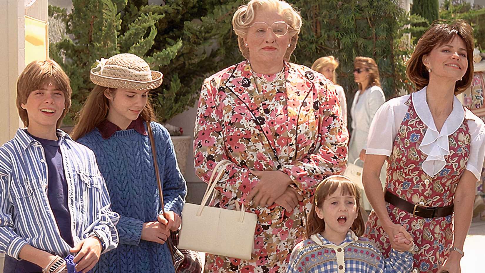 Daniel, dressed as Mrs. Doubtfire, standing with his wife and kids outside somewhere in Mrs. Doubtfire.