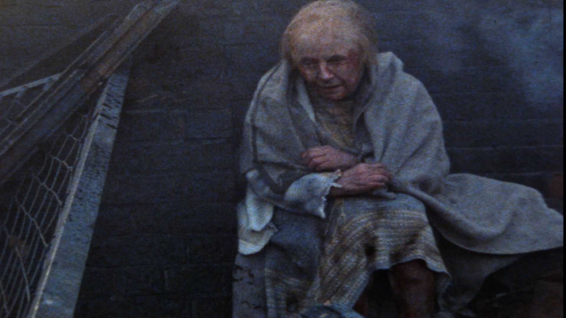 An older woman wrapped in a blanket with blood on her face in Threads