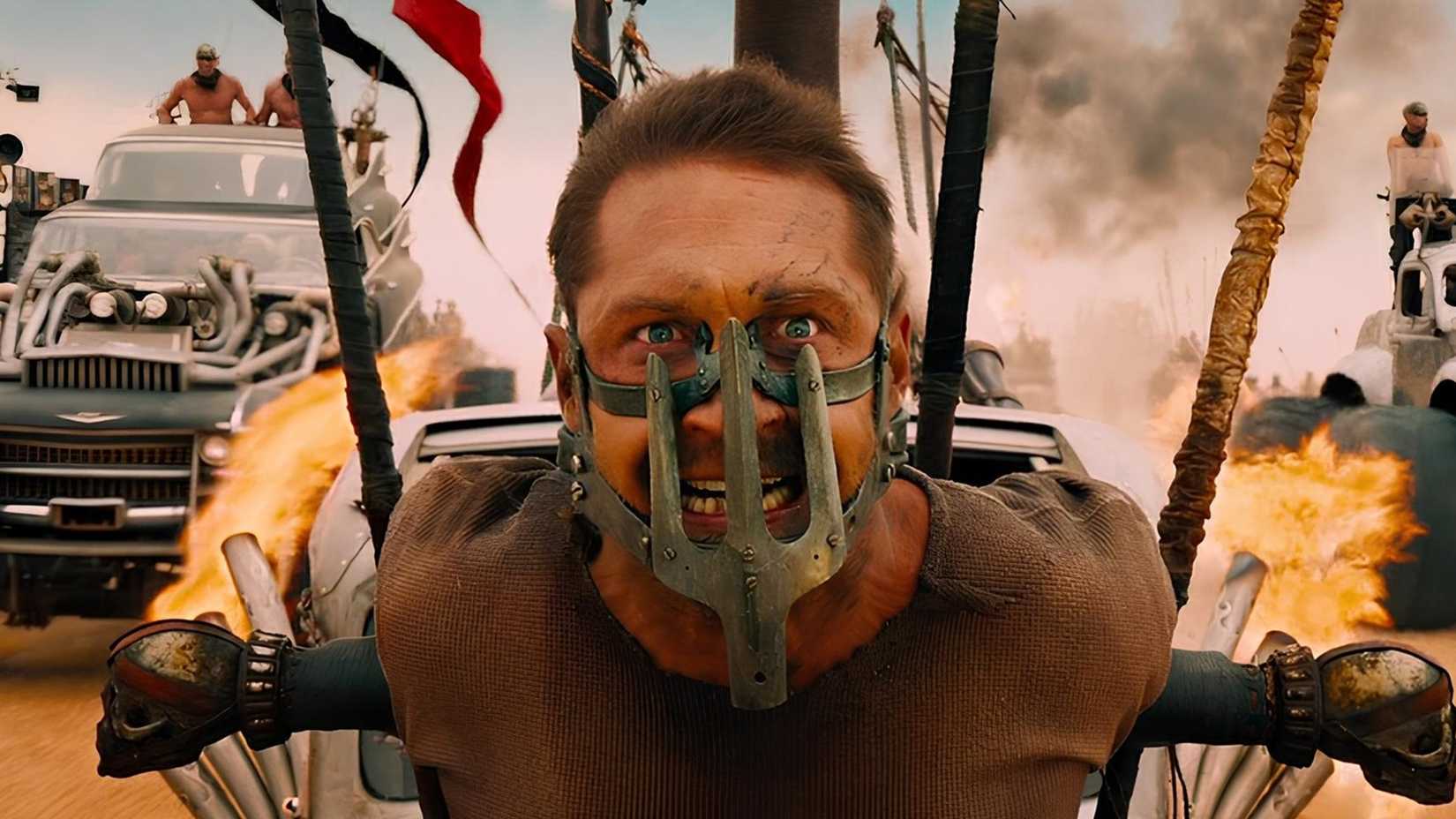 Tom Hardy in Mad Max Fury Road with a metal trap on his face as he is strapped to the front of a car