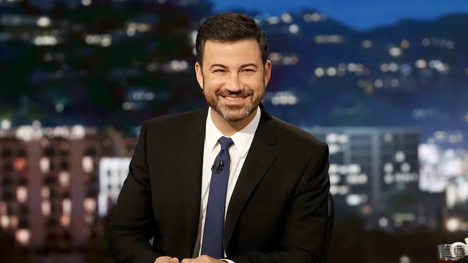Jimmy Kimmel sitting at his desk and smiling