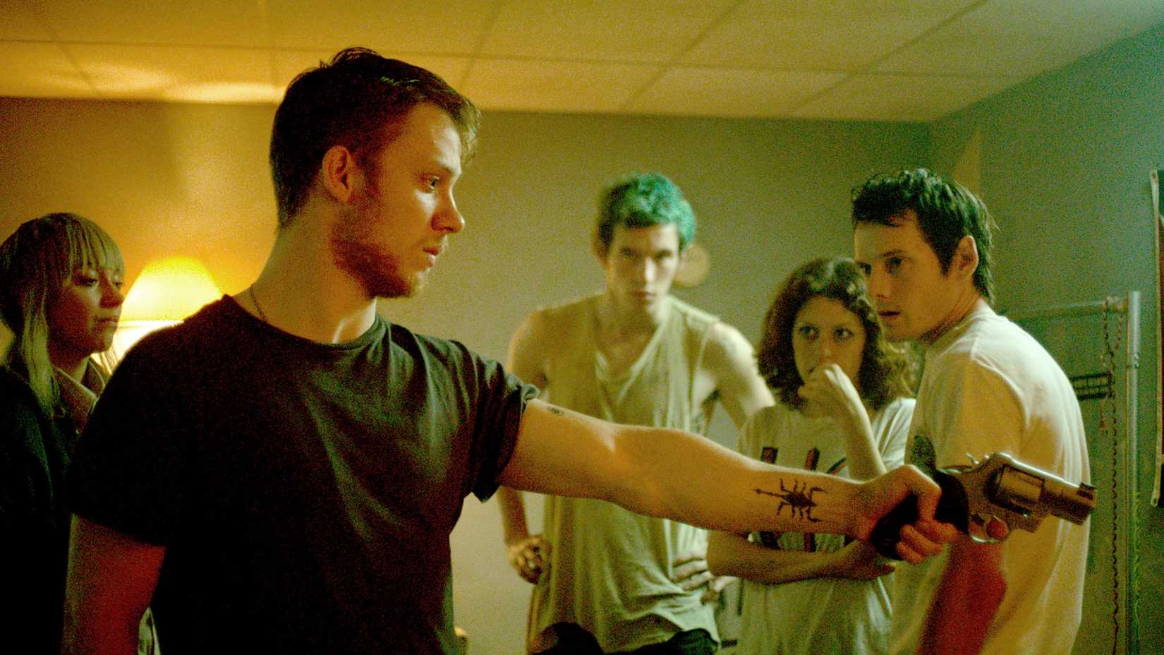 a man points a gun while others watch him in Green Room