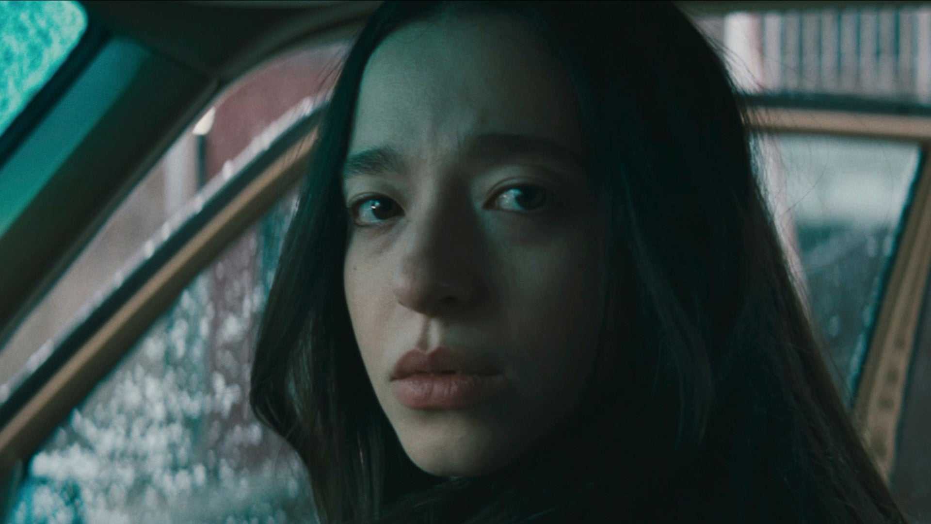Mikey Madison in Anora in a car looking to the side directly toward the camera