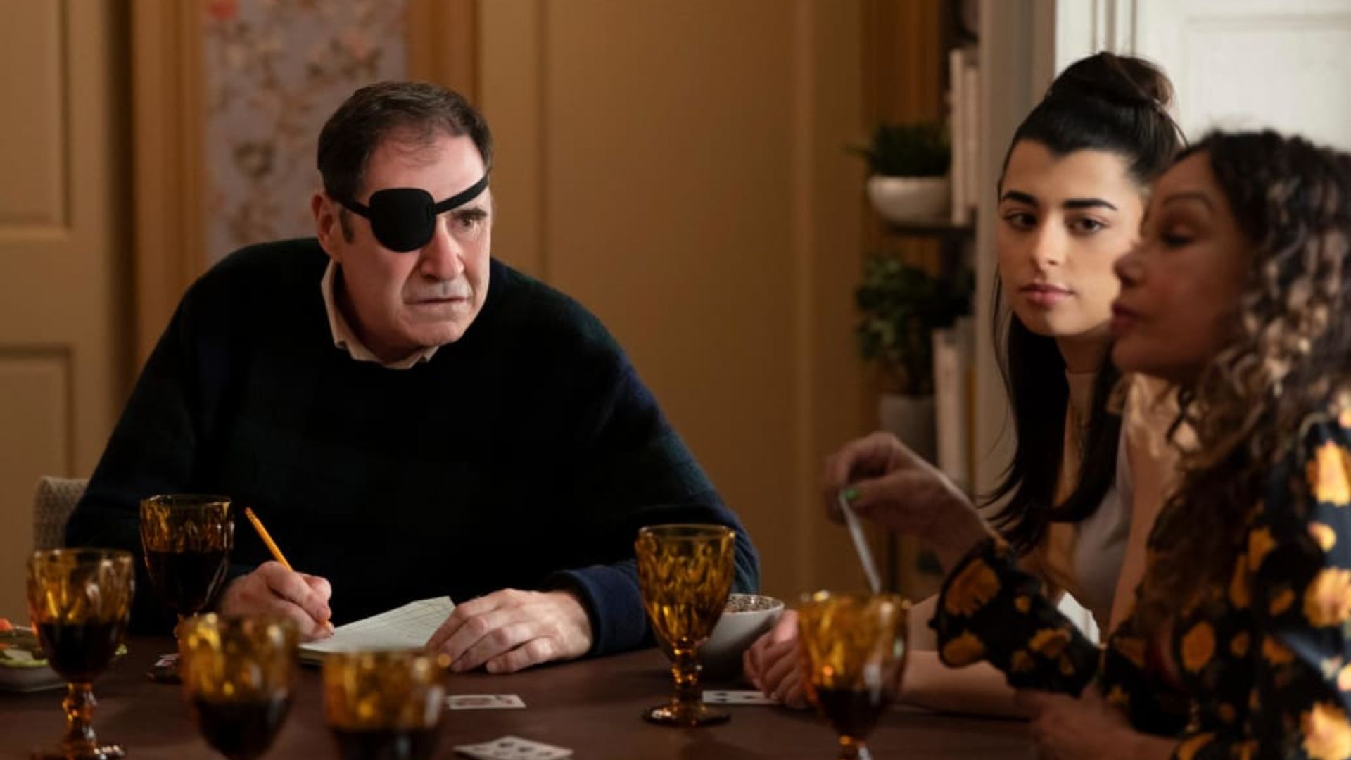 Richard Kind wearing an eye patch at a table with two women in Only Murders in the Building