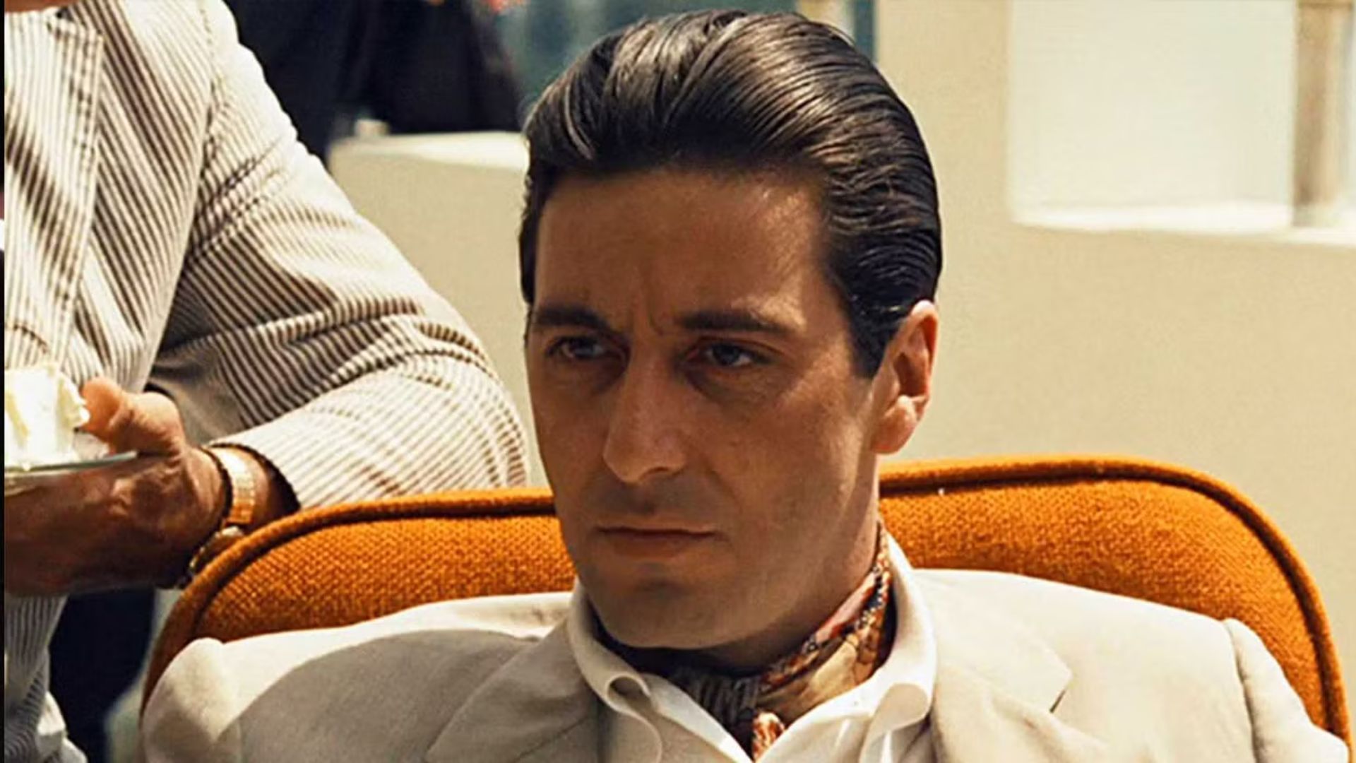 al pacino as michael corleone wearing a tan suit sitting in an orange chair in the godfather part ii 1