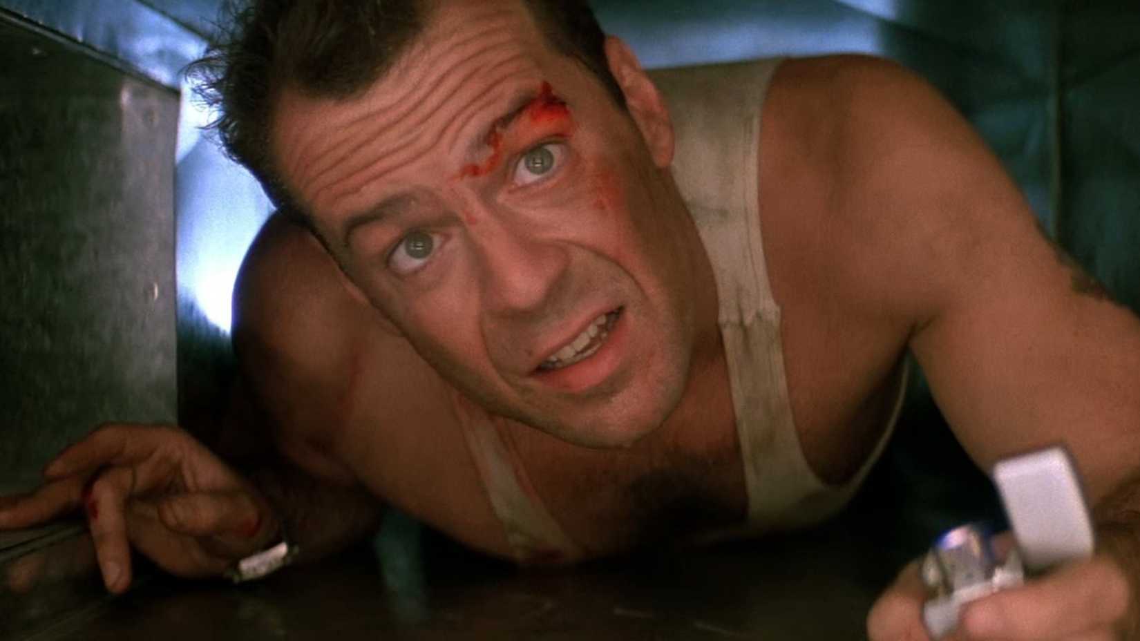 Bruce Willis as John McClane crawling through a vent while carrying a lighter, covered in blood, in Die Hard.