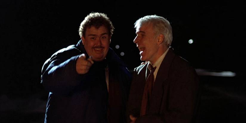 Steve Martin as Neal smiling and John Candy as Del laughing in Planes Trains and Automobiles.