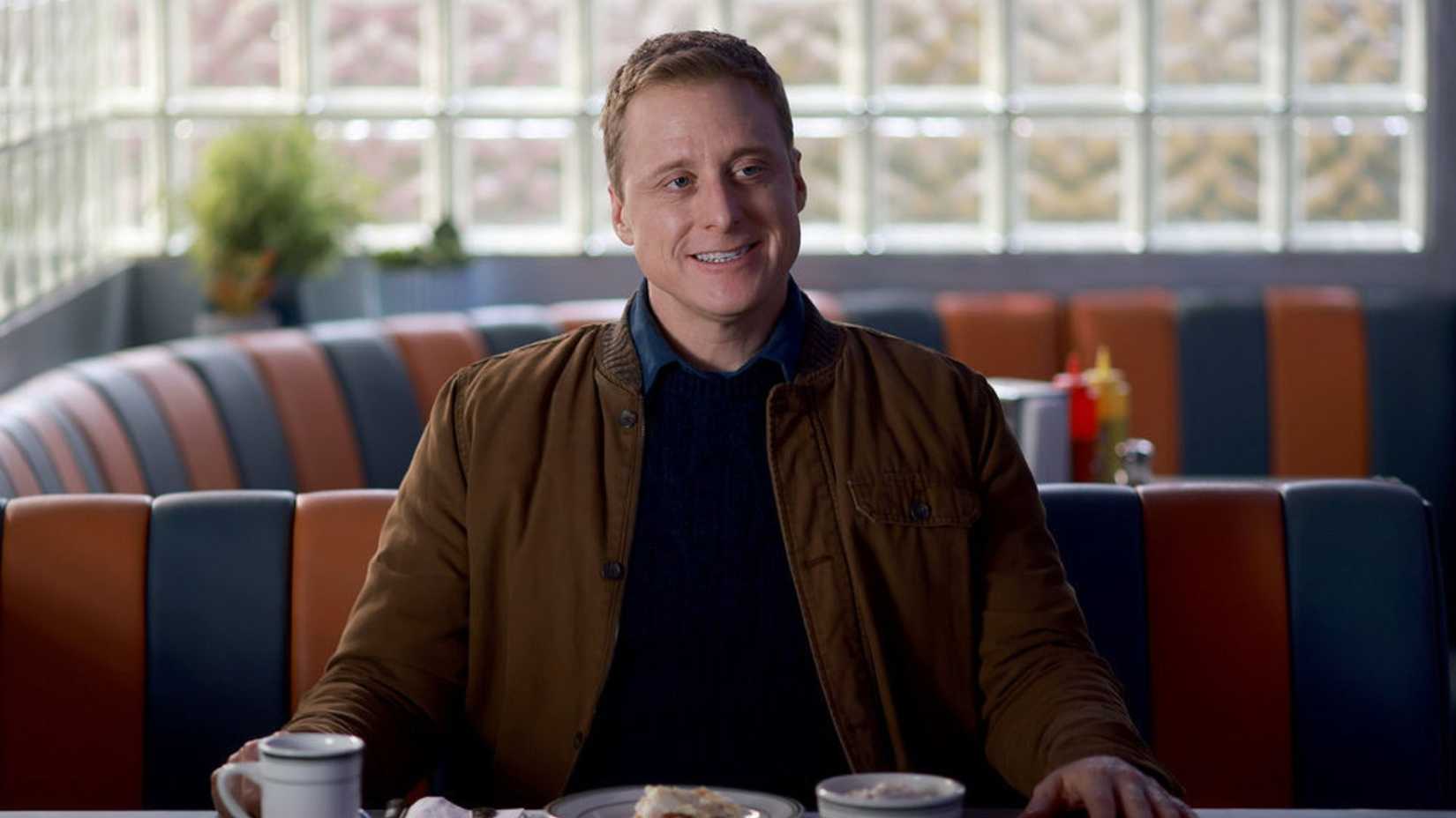 Alan Tudyk smiling at a table in the comedy series Resident Alien