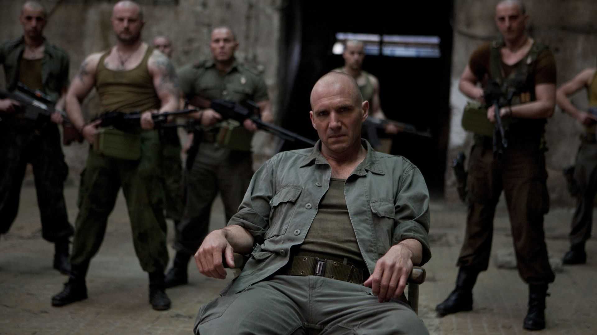Ralph Fiennes site on a chair with thugs behind him in Coriolanus (2011)