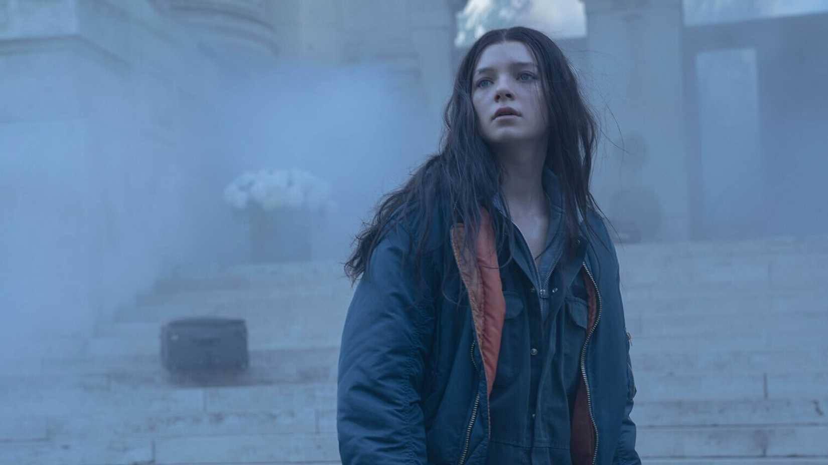 Esmé Creed-Miles standing on a staircase looking behind her in Hanna