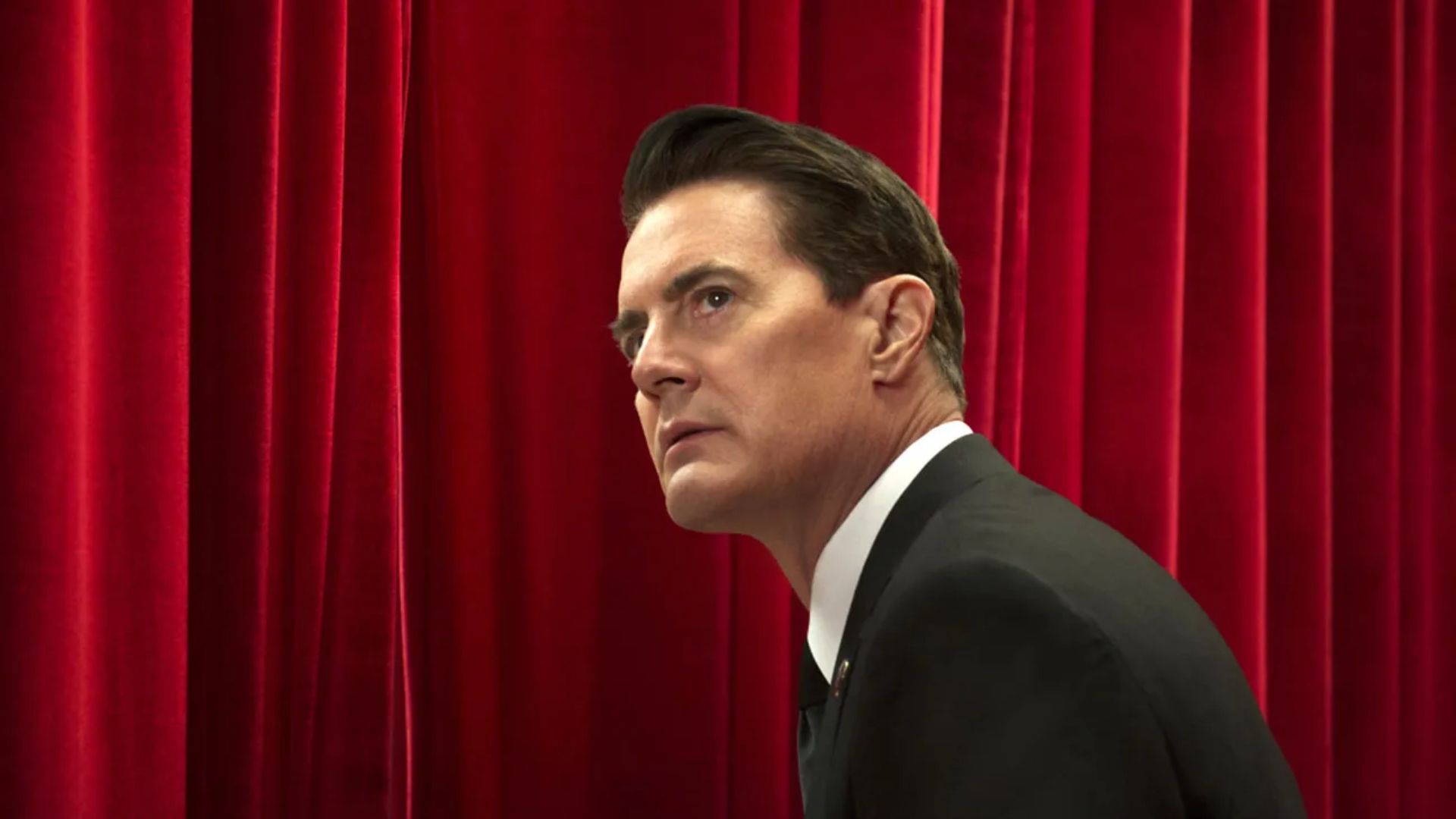 kyle maclachlan in a suit in front of red curtains in twin peaks the return