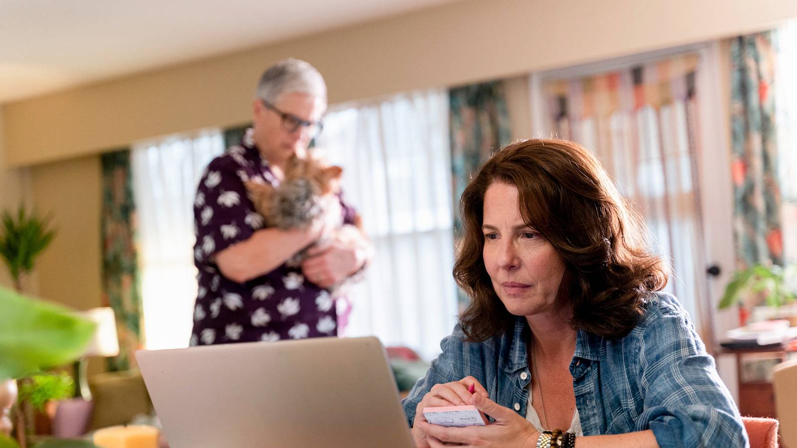 Teddi on the computer as Velma holds the dog in the background on Tracker. 