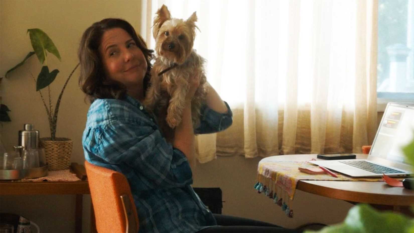 Teddi sitting at her desk in front of the computer holding up her dog on Tracker.
