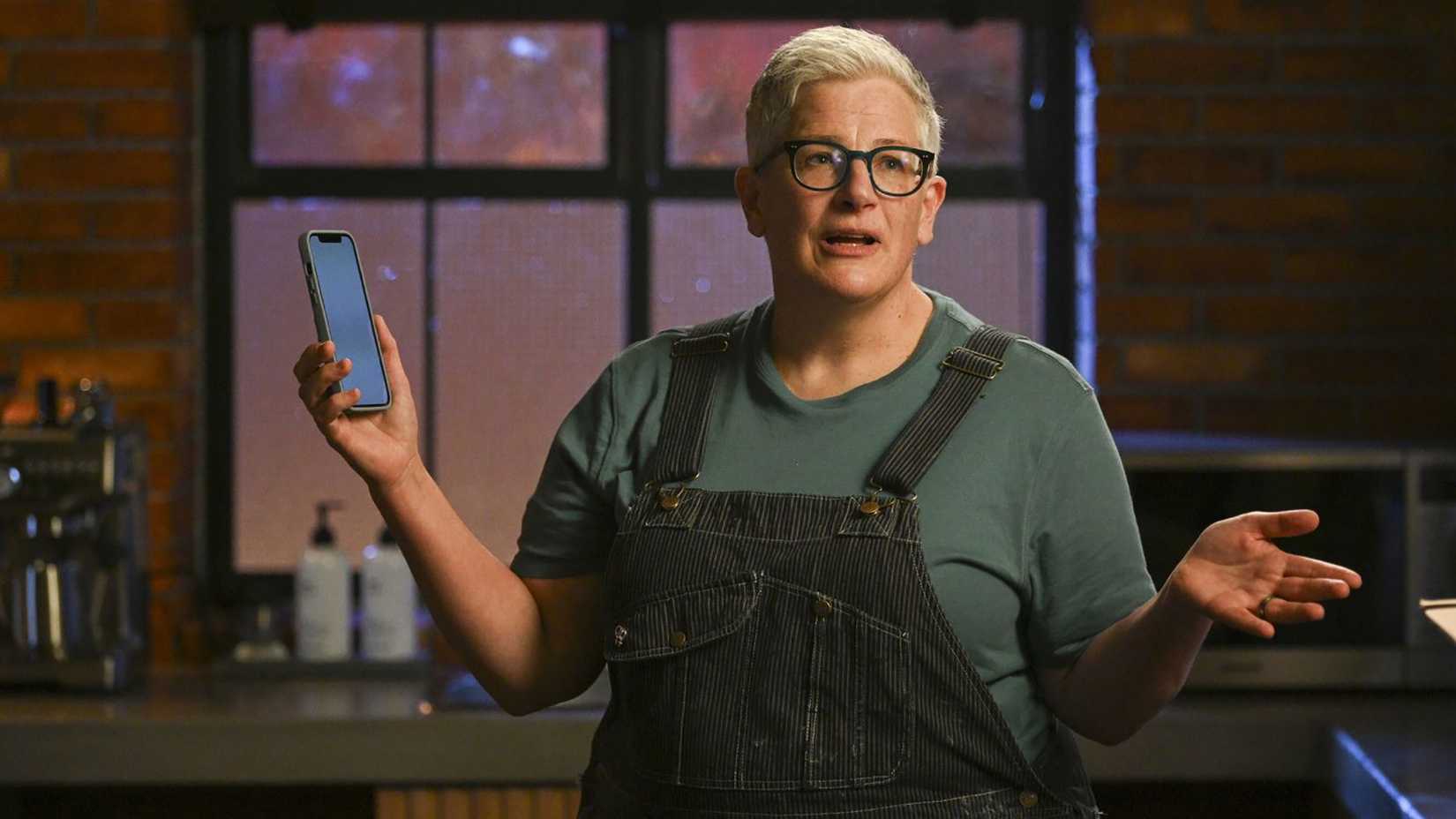 Velma in overalls holding out her hands, her phone in one of them on Tracker