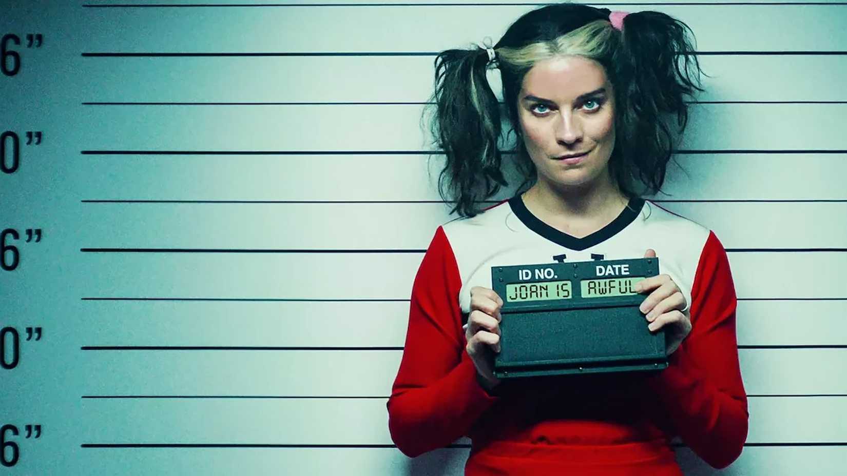 A woman in a cheerleading outfit with pigtails smirks for her mugshot in Black Mirror "Joan is Awful"