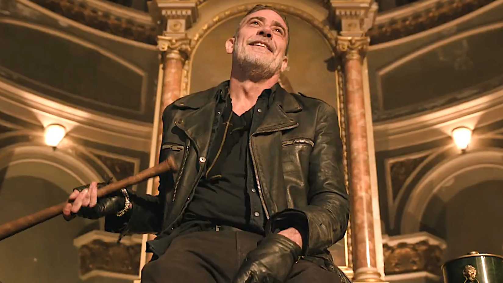 A shot from below of Negan smiling while holding a new bat in The Walking Dead: Dead City.