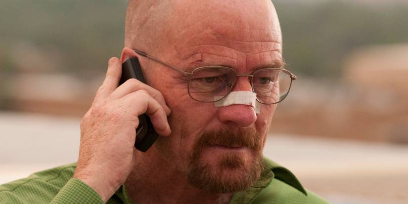 Bryan Cranston as Walter White wearing a bandage on his nose and talking on a phone in the street in Breaking Bad.