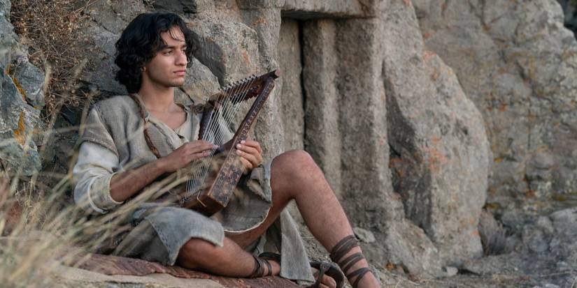 Michael Iskander sitting outside strumming a harp in House of David