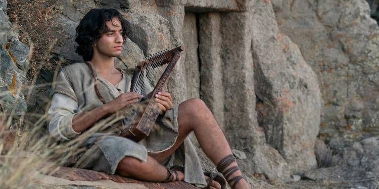 Michael Iskander sitting outside strumming a harp in House of David