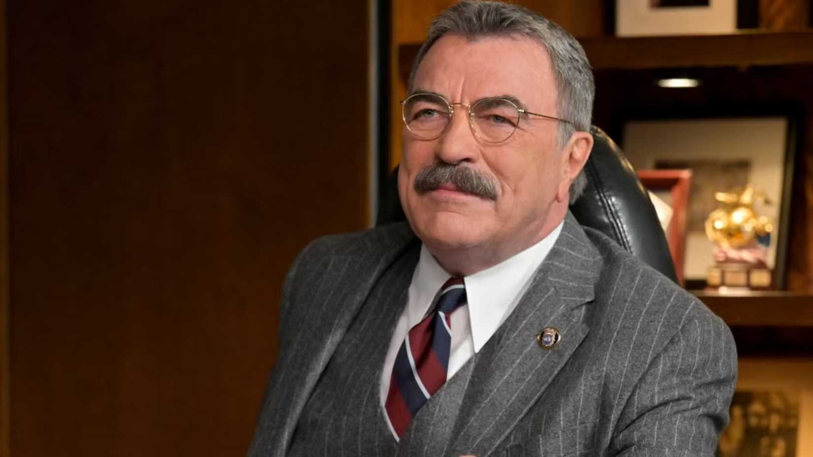 Tom Selleck in Blue Bloods sitting at his desk smiling