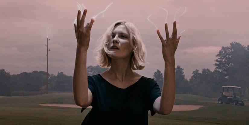 Kirsten Dunst in Melancholia with white wisps of energy coming out of.her fingers