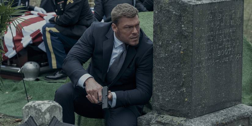 Alan Ritchson in Reacher kneeling by a grave with a gun