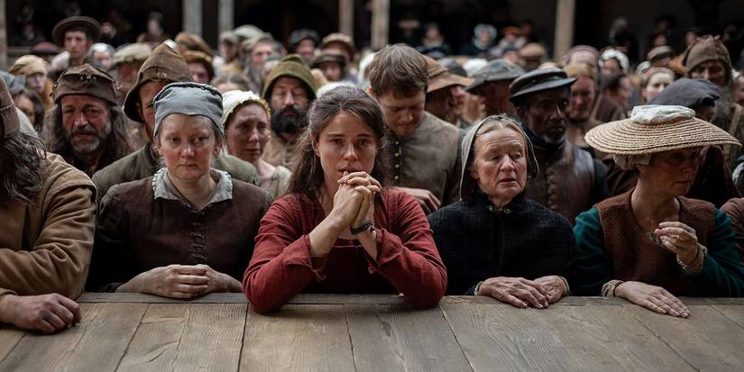 Jessie Buckley in Hamnet leaning on a wood floor praying