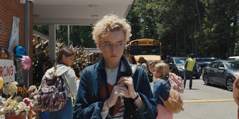 Julia Garner in Weapons walking outside of a school with a purse and kids behind her