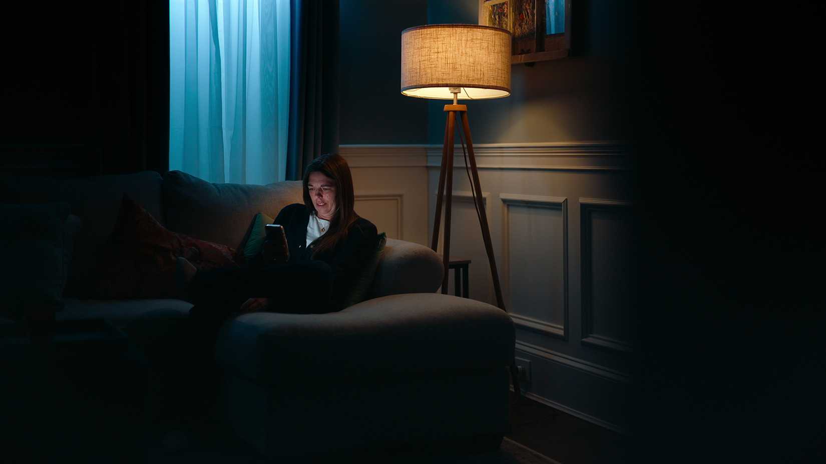 Kendra in the dark on the couch on her phone in Unknown Number: The High School Catfish.