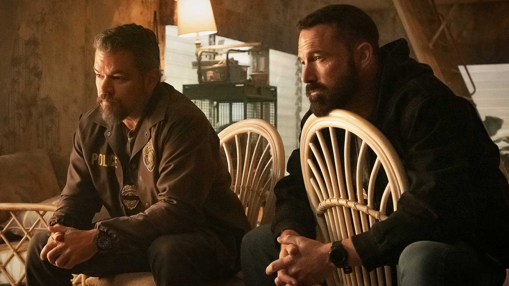 Ben Affleck and Matt Damon in The Rip sitting on chairs talking to someone off-screen