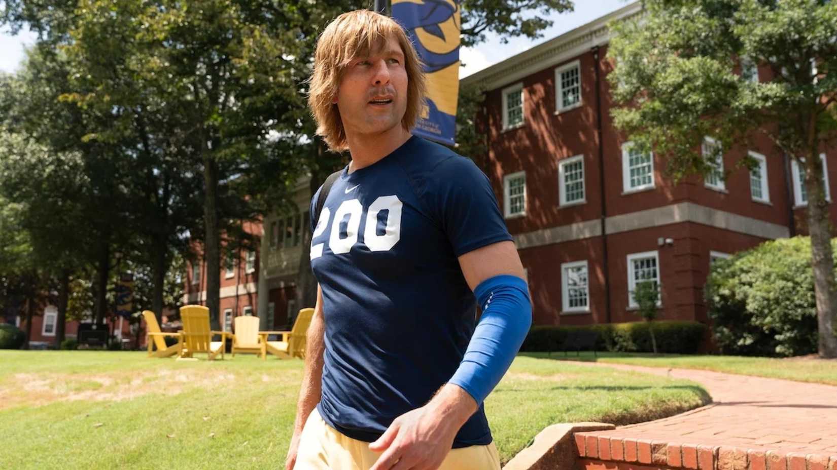 Glen Powell in Chad Powers walking on campus wearing an athletic shirt and arm sleeve
