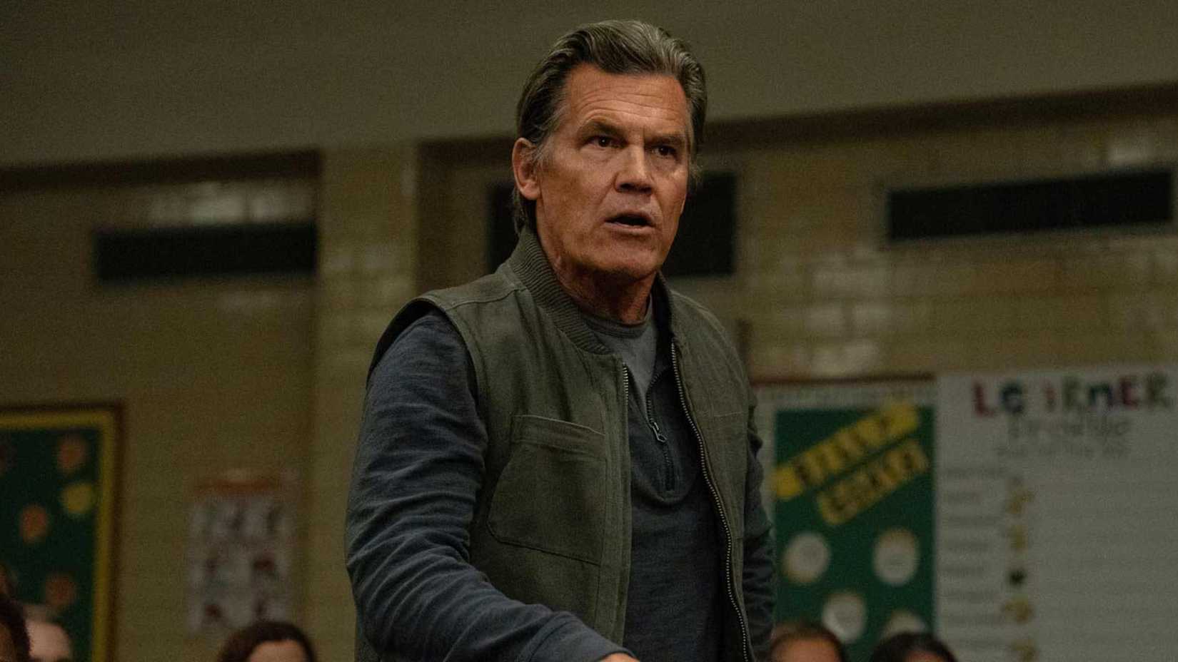 Josh Brolin in weapons in a town hall meeting standing up and speaking
