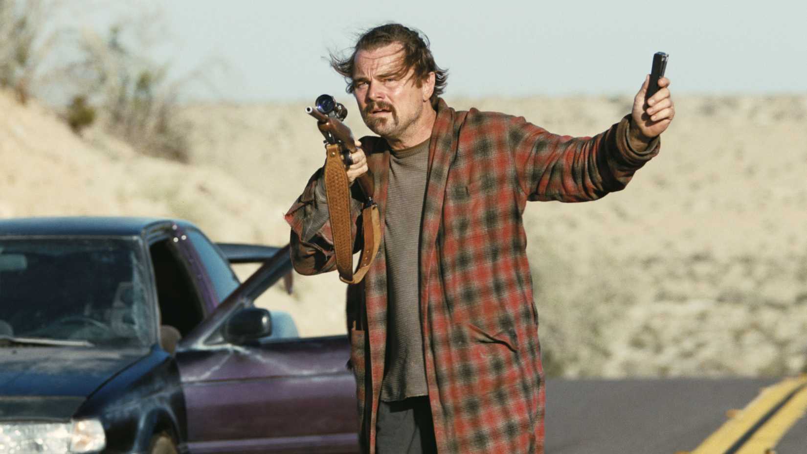Leonardo DiCaprio holding a rifle and device in One Battle After Another