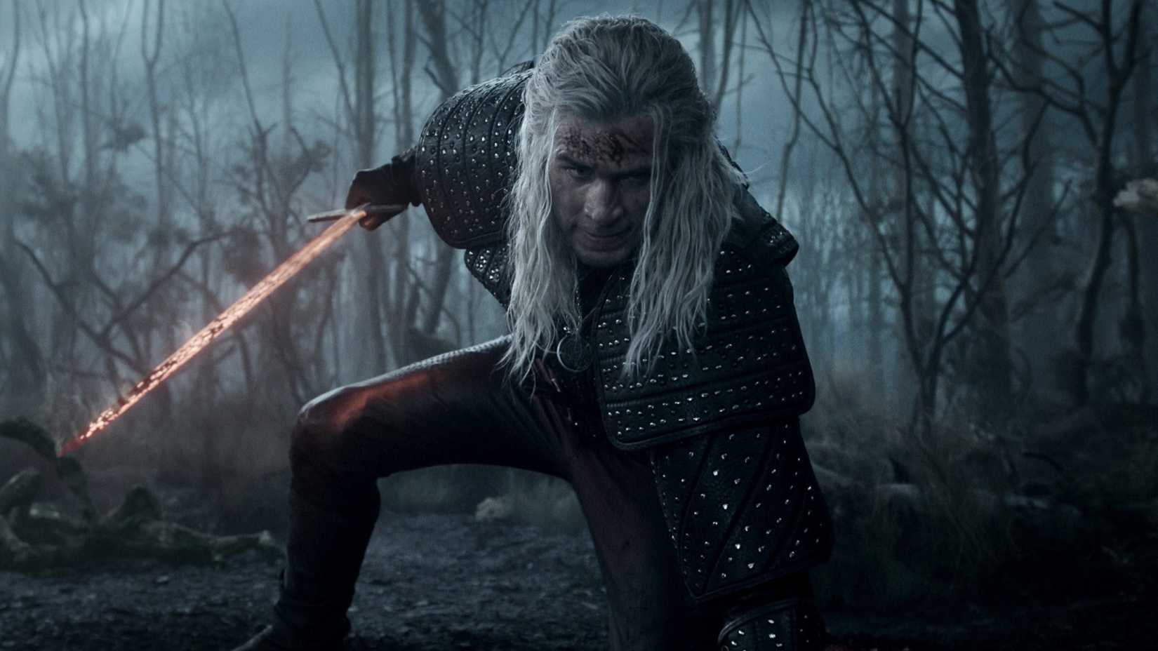 Liam Hemsworth in The Witcher holding a sword in a dead forest